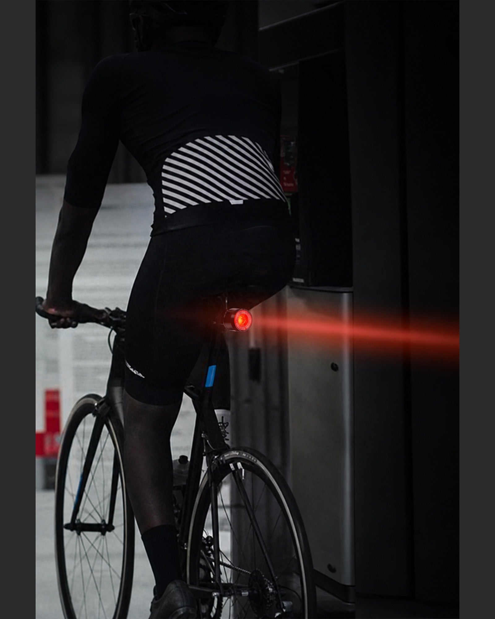 Cyclist viewed from behind with a red rear light beam extending across the road