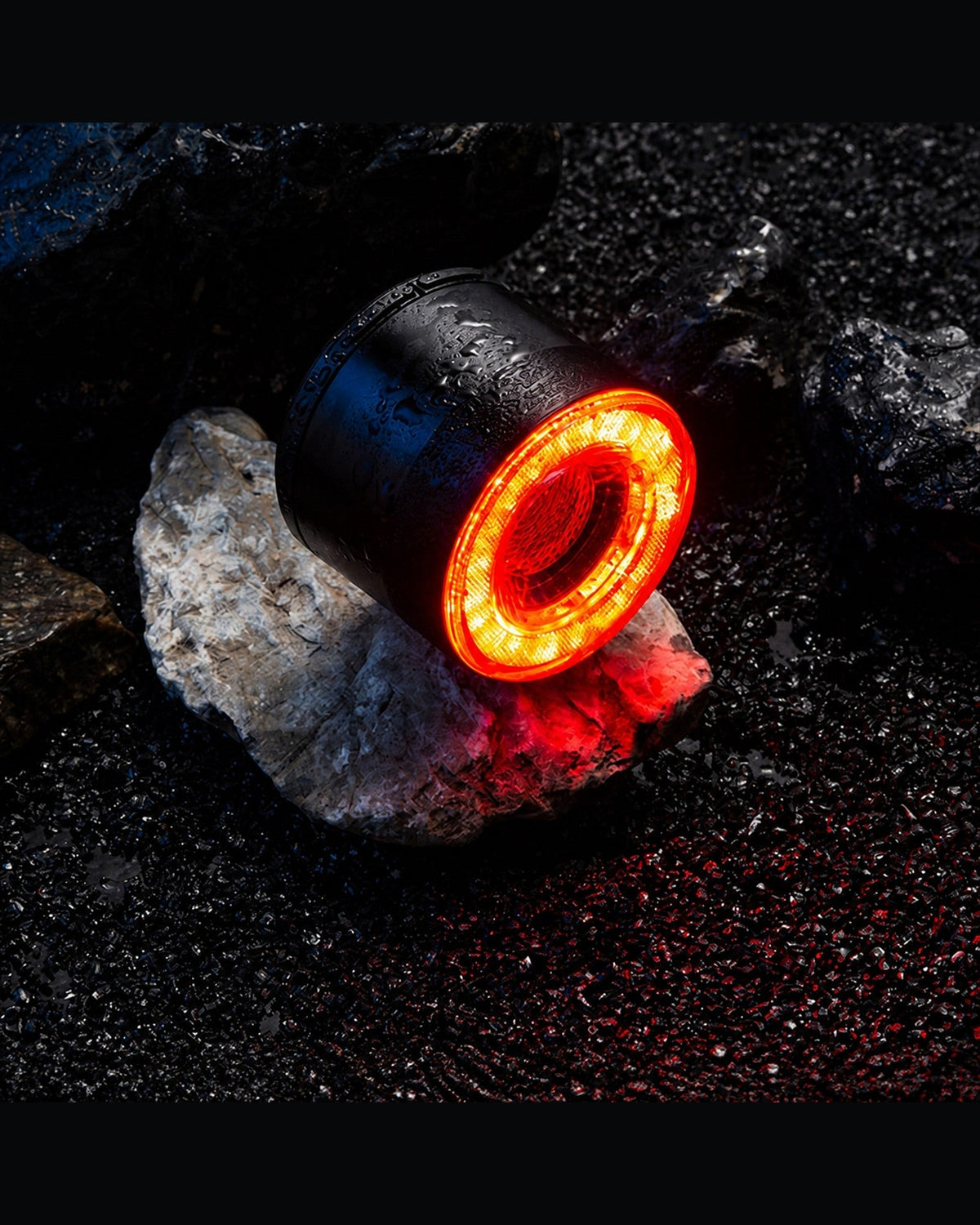 Round RGB halo bike light glowing red on wet rocks in a dark outdoor scene