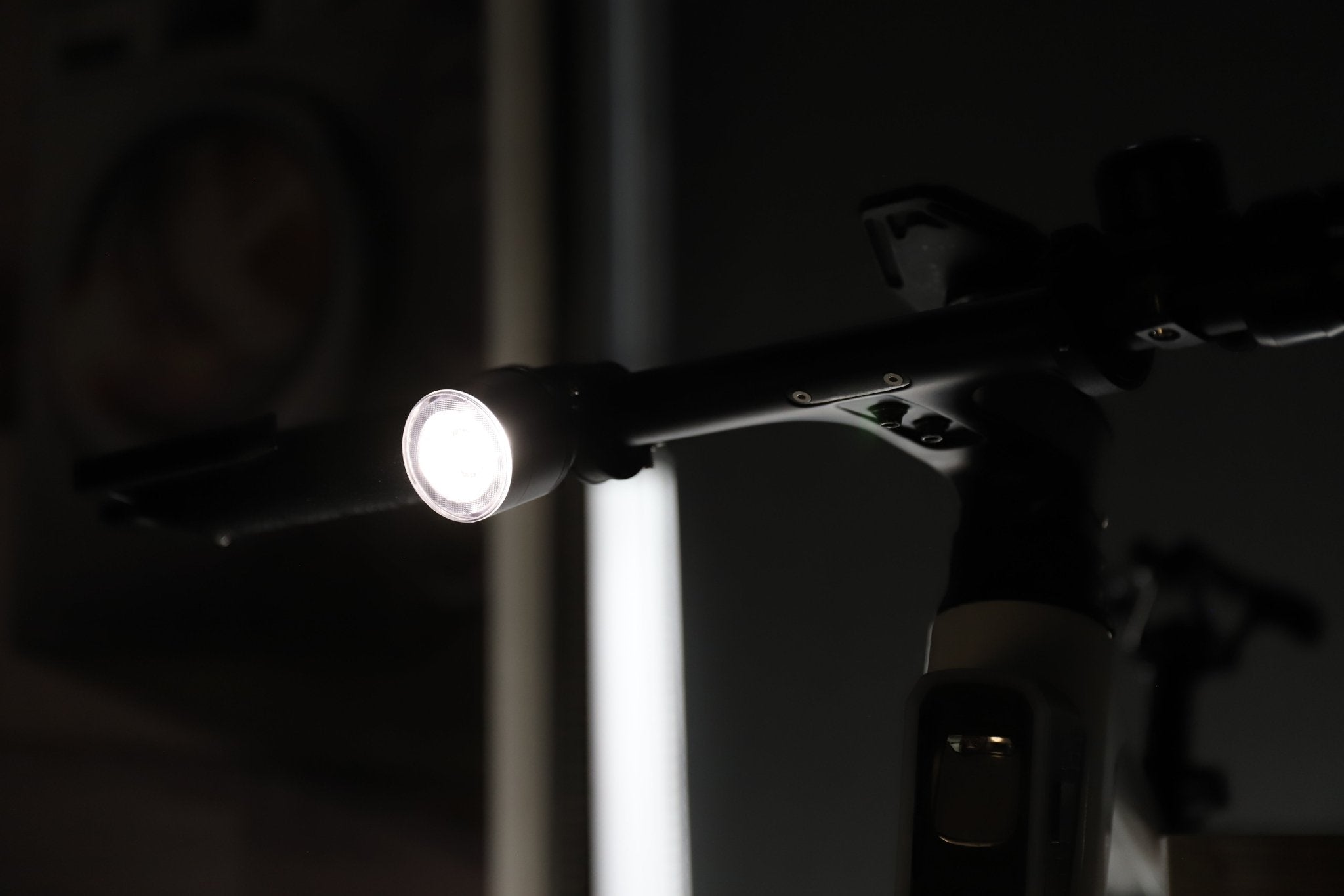 Handlebar-mounted bike light glowing white against a dark indoor background