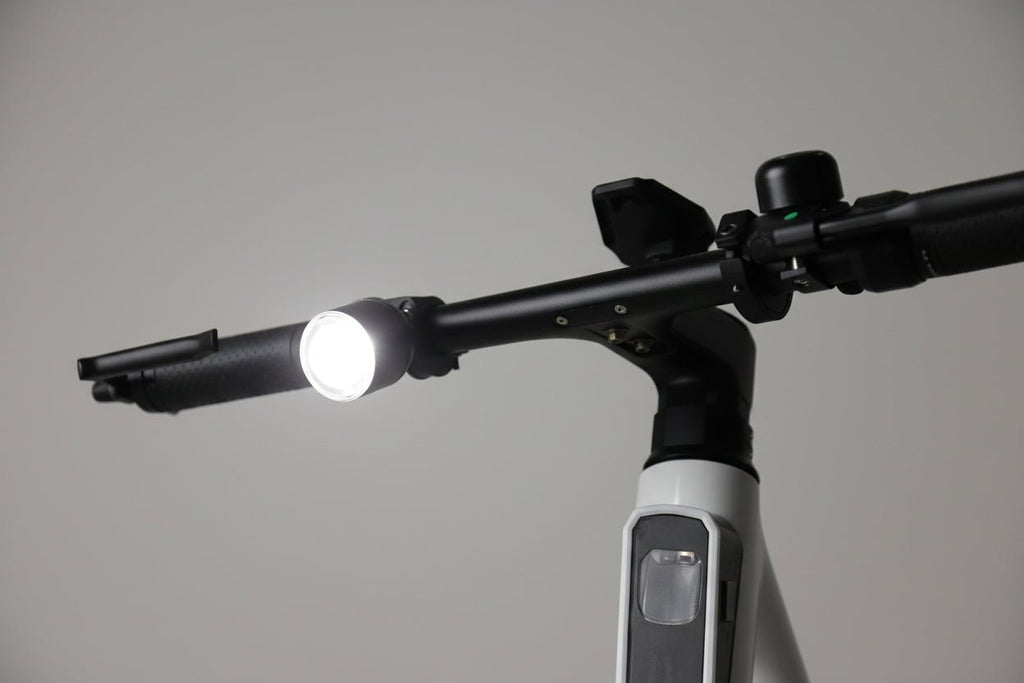 Handlebar-mounted bike light shining a bright white beam in a studio scene