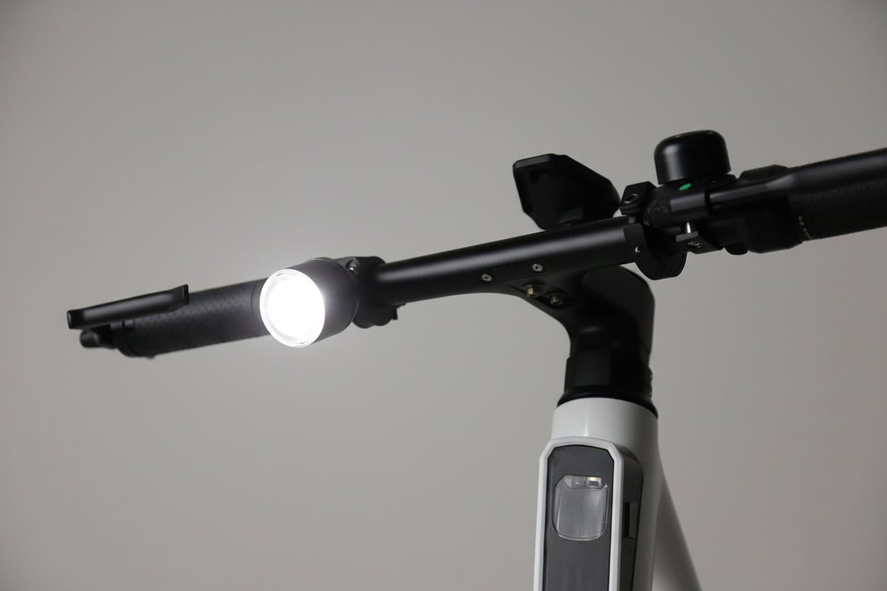 Handlebar-mounted bike light shining a bright white beam in a studio scene
