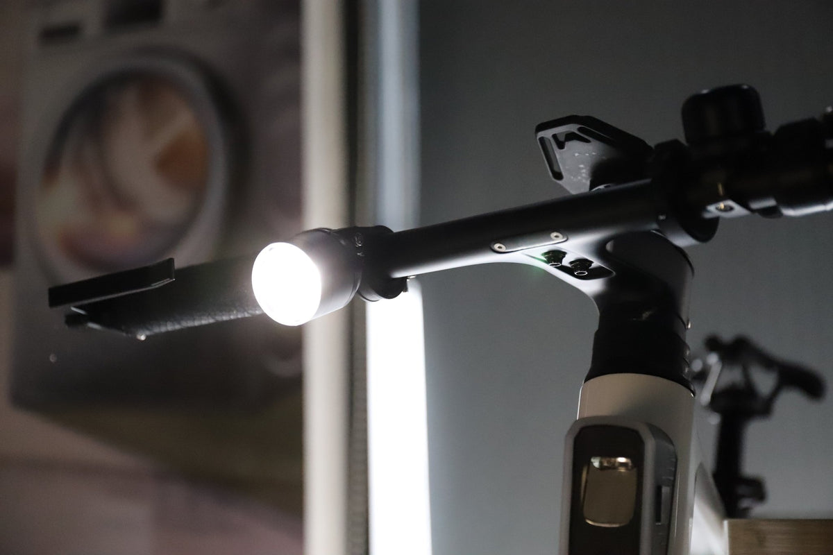 Handlebar-mounted bike light shining a bright white beam in a close-up scene